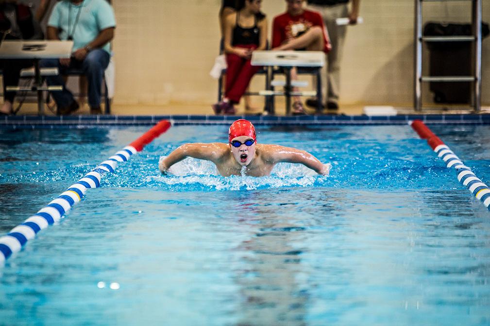 Schwimmer in roter Badekappe und Brille Brustschwimmen im blauen Schwimmbecken, Zuschauer im Hintergrund.