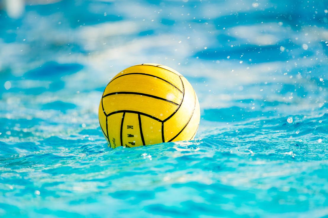 Gelber Wasserball schwimmt auf einer blauen Wasseroberfläche mit spritzendem Wasser im Hintergrund.